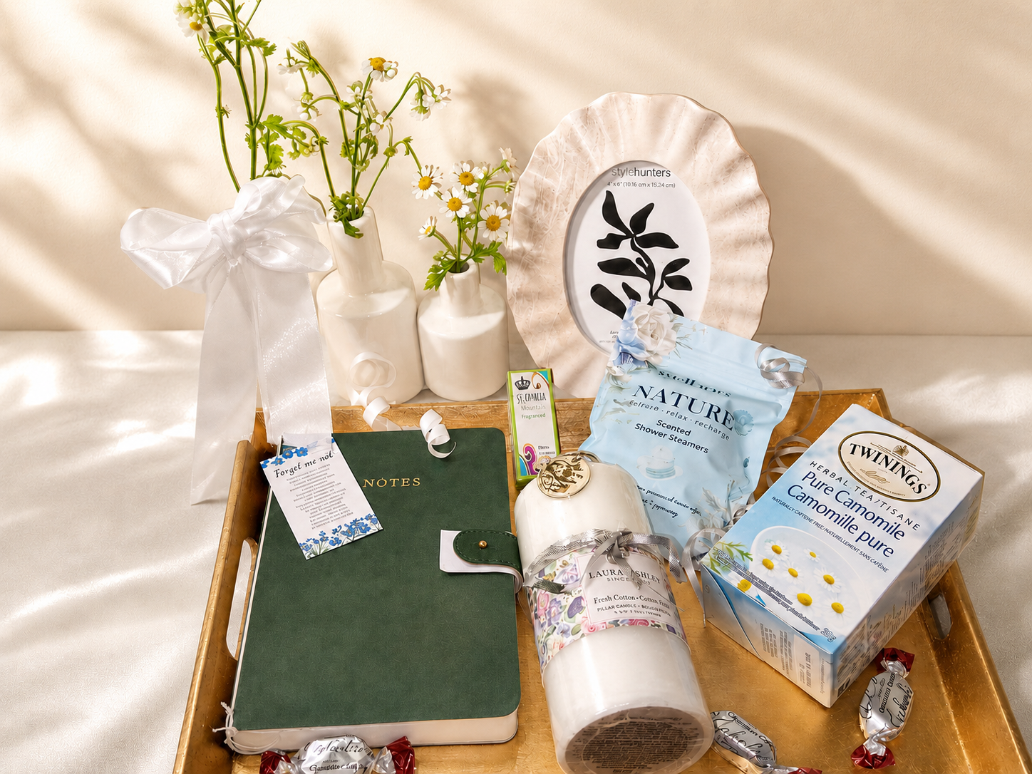 Editorial flat-lay of bereavement basket items &mdash; candle, journal, tea, daisies